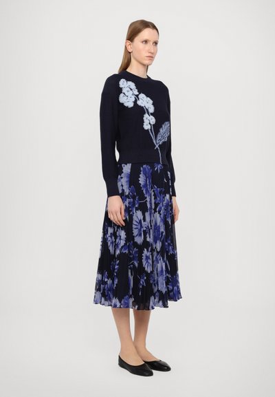 Navy sweater with light blue floral embroidery, paired with a pleated floral skirt in varying shades of blue and black; flat black shoes.