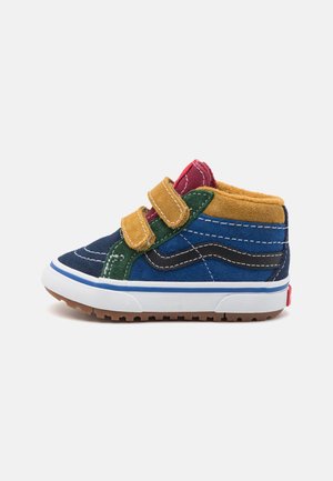 Zapatilla de caña alta para niño pequeño con paneles de ante azul, verde, mostaza y rojo, suela de goma blanca, tiras de velcro y suela exterior marrón estriada.