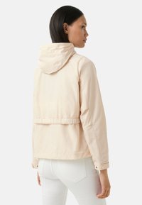 Veste à capuche beige clair avec une taille cintrée, des manches longues et une texture lisse et mate. Design simple sans motifs ni matériel visible.