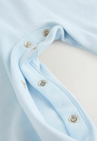 Lyseblåt bomuldsplagg med ribbet kant og sølvfarvede lynlås-knapper langs åbningen, der fremhæver en blød tekstur og enkelt design.