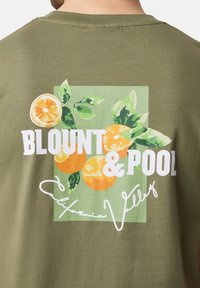 Oliven grøn t-shirt med et grafisk print af appelsiner og blade. Har hvid tekst, der står "BLOUNT & POOL California Valley."