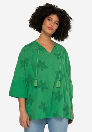 Grøn bomuldsbluse med V-hals, trekvartærmer og blomsterbroderi. Har frynsesnore og et løst, flydende design.