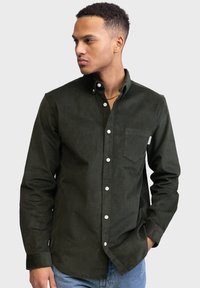 Donkergroen corduroy knoopshirt met een borstzak, witte knopen en een standaardkraag. Soepele textuur en een aansluitende pasvorm.