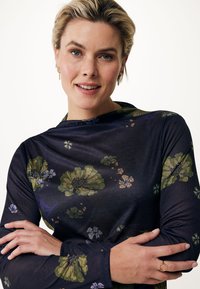 Långärmad blommig blus i mörk marinblått, med gröna och lila blommor. Slät, lättviktig tyg med avslappnad passform och hög hals.