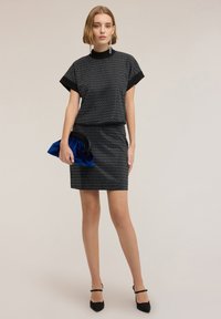 Czarny zestaw sukienki składający się z krótkiego topu z krótkimi rękawami i dopasowanej spódnicy, obie zdobione wzorem diamentu, zestawione z niebieską kopertówką.