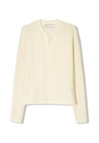 Top de manga larga color crema claro con textura de rayas verticales, tapeta abotonada y cuello redondo. El corte es ligeramente corto y tiene aberturas laterales.