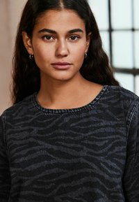 Sweatshirt noir avec un motif zèbre subtil, col rond et tissu texturé, présentant une coupe décontractée et des détails de surpiqûres visibles.