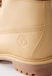 Acercamiento de una bota de cuero marrón con un logo de árbol en relieve y costuras detalladas sobre una suela de goma resistente.