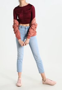 Burgundské zkrácené tričko s nařasením, růžová bomber bunda, světlé modré skinny džíny a světle růžové tenisky vytvářejí vrstvený ležérní vzhled.