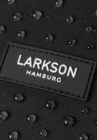 Fekete textúrájú szövet, kiemelkedő kör alakú részletekkel és egy fehér logóval, amelyen az áll: "LARKSON HAMBURG."