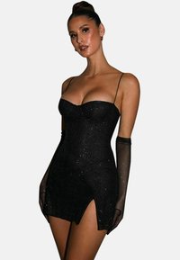 Robe mini noire à sequins avec un design ajusté, décolleté en cœur, fines bretelles et fente sur le côté. Accompagnée de gants transparents noirs.
