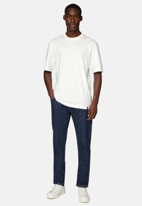 Bela bomba majica iz bombaža z okroglim izrezom in kratkimi rokavi, v kombinaciji s temno modrimi kavbojkami in belimi športnimi čevlji. Enostaven in sproščen dizajn.