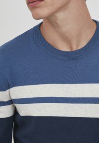 Kék környakú pulóver vízszintes fehér és világoskék csíkokkal. Puha anyagból készült, bordázott nyakkal és mandzsettákkal.