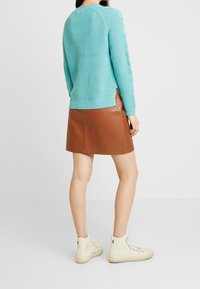 Pull turquoise en maille avec des accents côtelés, associé à une mini-jupe en cuir marron et des baskets montantes crème.