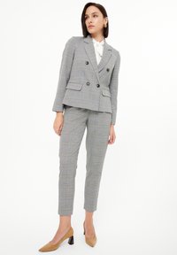 Conjunto de traje de cuadros gris que incluye un blazer de corte cruzado con botones a tono y pantalones slim-fit a juego. Combinado con una blusa blanca y tacones beige.