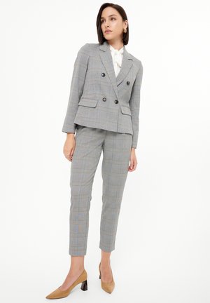 Šedý kostkovaný oblek obsahující dvouřadý blazer s tónovanými knoflíky a odpovídajícími slim-fit kalhotami. Nosit s bílou blůzou a béžovými podpatky.