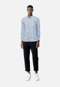 Camicia a maniche lunghe di un blu chiaro con motivo floreale, abbinata a pantaloni neri a sigaretta e sneakers bianche. Tessuto morbido con colletto a bottoni.