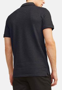 Donkergrijze polo met korte mouwen, geribbelde kraag en subtiele textuur. Heeft zijsplitten en een klein logolabel aan de onderkant.