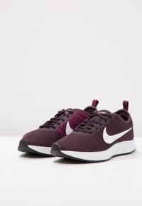 Nike juoksukengät, joissa on viininpunainen verkko-osa, valkoinen logo ja valkoinen välikenkä. Sisältää violetteja yksityiskohtia ja tekstuurilla varustetun pohjan.