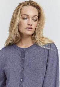 Lilla kudumine kardigan ümmarguse kaelusega, ees nööpidega sulgemine, mustade nööpidega ja plaatide peal rombikujulised aktsendid.