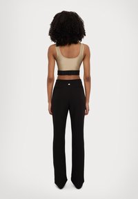 Top corto marrone con una larga fascia elastica nera con testo, abbinato a pantaloni aderenti neri, entrambi realizzati in tessuto liscio ed elastico.