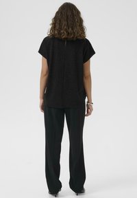Top negru texturat cu mâneci scurte și o cusătură centrală pe spate, asortat cu pantaloni negri cu talie înaltă, având o croială lejeră.