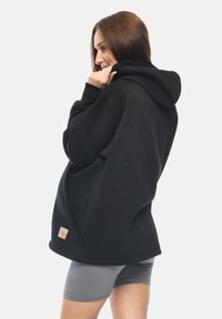 Felpa nera con cappuccio realizzata in morbido tessuto felpato, con vestibilità rilassata, tasca a marsupio e un piccolo etichetta del marchio sull'orlo inferiore.