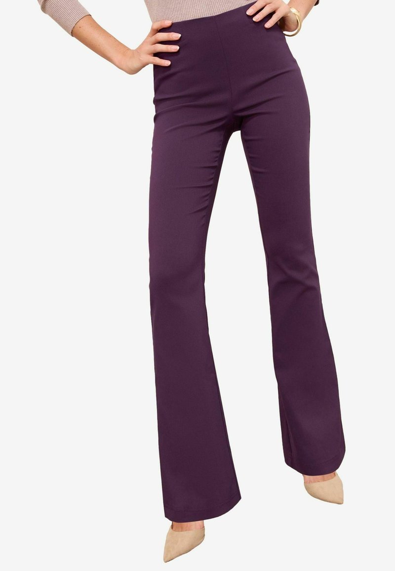 Uitlopende broek van diep paarse stof met een gladde afwerking en een hoge taille. Gecombineerd met lichtgekleurde puntige hakken.