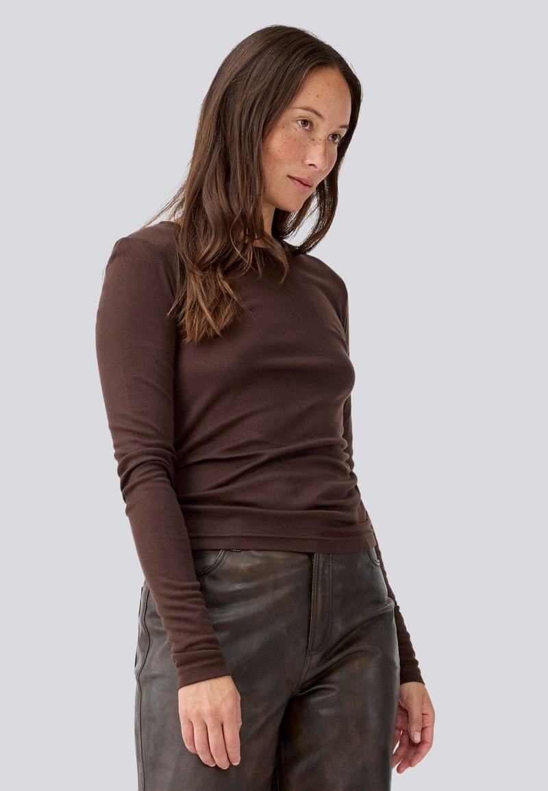 T-shirt marrone a maniche lunghe in materiale morbido con design aderente, scollatura a girocollo e polsini senza cuciture, abbinato a pantaloni in pelle nera.