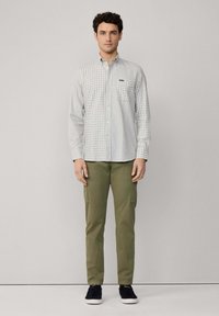 Camisa de cuadros en gris claro y verde con un bolsillo en el pecho, combinada con pantalones cargo en verde oliva y zapatillas negras.