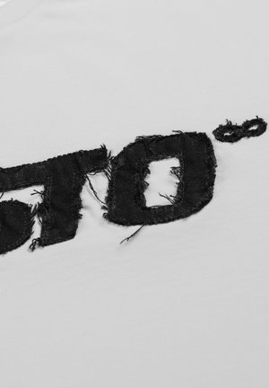 Biała bawełniana koszulka z czarnym, postarzanym wzorem z frędzlami, prezentująca stylizowany tekst i okrągły akcent.