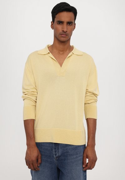 Gelber gestrickter Pullover mit einem Kragen, langen Ärmeln und gerippten Bündchen. Trägt man über dunkelblauen Jeans mit einer lässigen Passform.