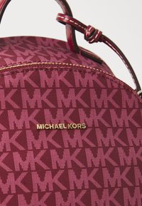 Zaino in tessuto bordeaux con un motivo geometrico di loghi MK interconnessi, logo Michael Kors in tono oro e chiusura superiore con zip.
