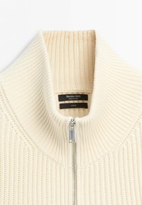 Cream ribbed knit sweater with a standing collar and silver zipper, showing Massimo Dutti brand label and cotton fabric tag.