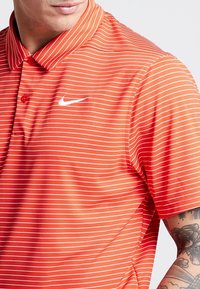 Rödrandig polo t-shirt med krage, med en vit Nike-logotyp på vänster bröst. Gjord av mjukt, andningsbart tyg.