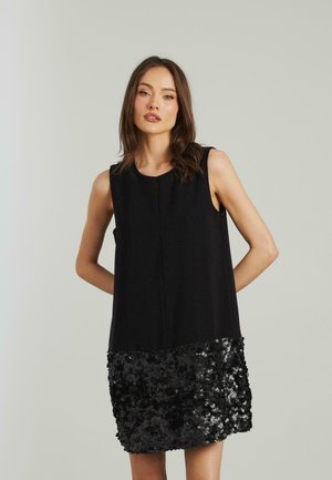 Black sleeveless dress with a smooth top and a textured, sequined hem in black, featuring a subtle front seam detail.