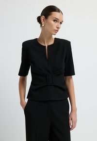 Top nero a maniche corte con scollatura rotonda, caratterizzato da un'apertura frontale e una fibbia decorativa in vita per un tocco di originalità.