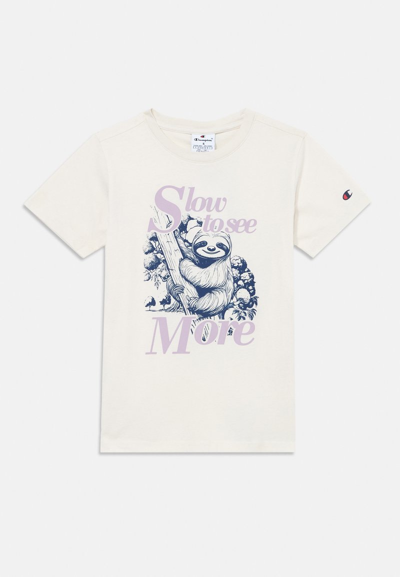 T-shirt de algodão de cor creme com uma ilustração de um bicho-preguiça azul e texto roxo que diz "Lento para ver mais." Mangas curtas, decote redondo.