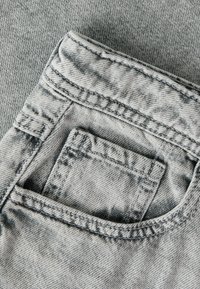 Gros plan sur un jean en denim gris clair montrant une poche avant avec une petite poche à monnaie à l'intérieur et des détails de couture visibles.