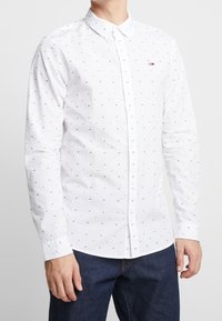 Camicia bianca con bottoni, decorata con piccoli punti stampati multicolori. Presenta un colletto classico e maniche lunghe. Include un dettaglio con il logo sul petto.