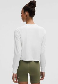 Valge pikkade varrukatega pluus, millel on lühendatud disain, sile tekstuur ja mansettidega varrukad, koos oliivroheliste lühikeste pükstega. Ilma nähtavate mustrite või aktsentideta.