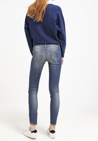 Sudadera de color azul marino, con textura, de cuello redondo y mangas raglán, combinada con jeans ajustados de color azul claro, que presentan bolsillos parche y un acabado desgastado.