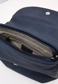 Åben navy blå læderhåndtaske, der viser en beige stofindvendig med prikker og et lynlåslomme indeni.