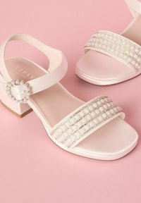 Sandalias de satén blanco con punta abierta y tacón grueso, que cuentan con tres filas de acentos de perlas y una hebilla decorativa con perlas en la correa del tobillo.