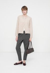 Cárdigan de punto color beige claro con cuello redondo y botones, combinado con pantalones grises de corte ajustado y mocasines burdeos brillantes. Bolso marrón.