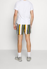 Moniväriset raidalliset uimapuvut, joissa on keltaisia, vihreitä, purppuranvärisiä ja valkoisia pystyraitoja; yhdistetty yksinkertaiseen valkoiseen T-paitaan ja tennareihin.