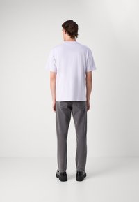 T-shirt blanc à manches courtes et col ras du cou associé à un jean gris à jambes droites et des chaussures noires, vu de dos.