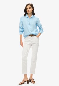 Jasnoniebieska koszula z długim rękawem z lekkiego materiału, białe spodnie proste, oraz brązowe sandały na obcasie z paskami. W zestawie brązowy pasek.