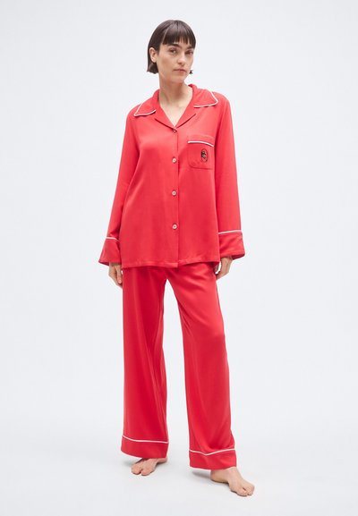 Σετ πιτζάμες από κόκκινο σατέν που περιλαμβάνει πουκάμισο με κουμπιά και λευκή διακοσμητική ραφή, τσέπη στο στήθος και παντελόνι με φαρδιά μπατζάκια. Λεία υφή, άνετη εφαρμογή.