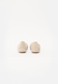 Mocassins en suède beige avec un design à bout rond, une semelle plate et des détails de couture minimalistes à l'arrière. Texture lisse sur l'ensemble.